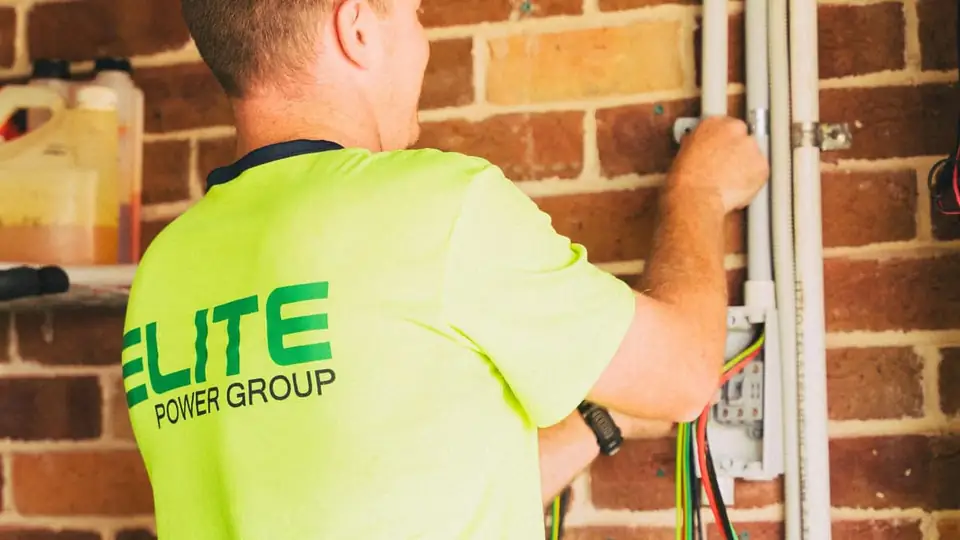 A hi-vis electrician wiring a meter box on a brick wall