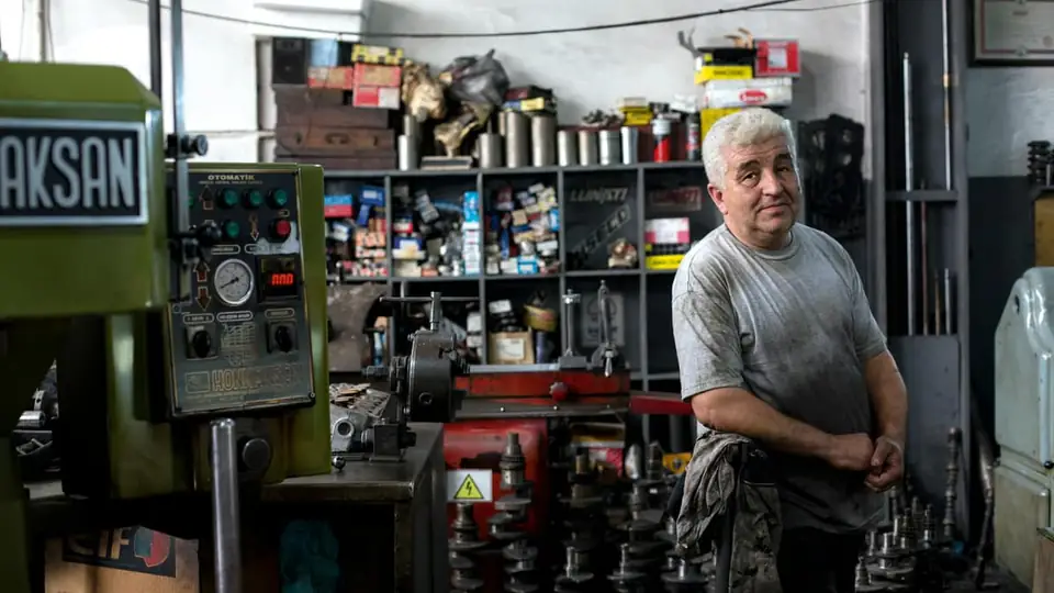 A mechanic standing in a busy workshop surrounded by parts