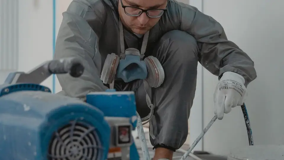 A painter in a respirator using a paint sprayer indoors
