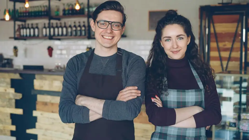 Two smiling cafe owners in aprons behind the counter